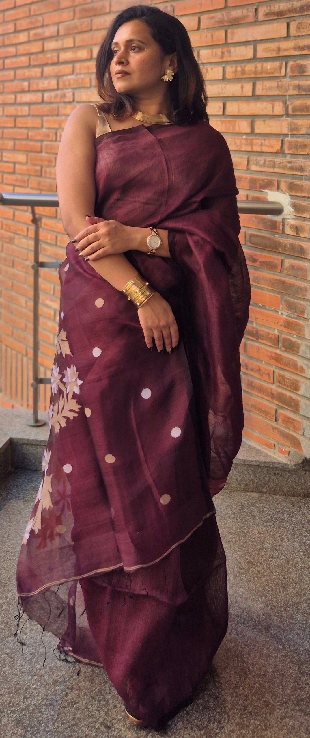 Woman in a maroon saree standing on a balcony with a cityscape view.