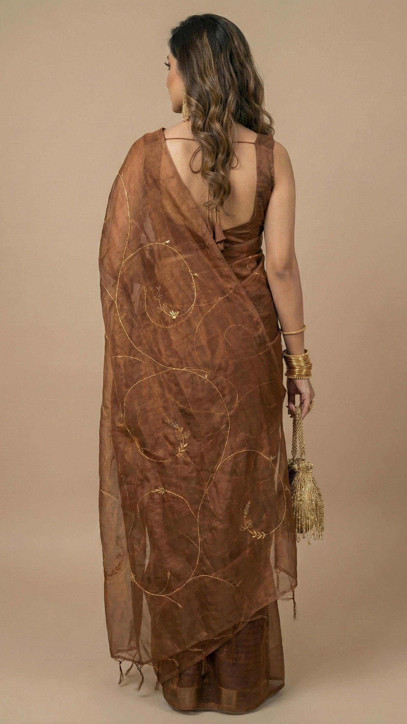 Woman wearing a brown saree with intricate designs against a beige background