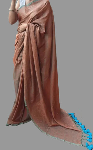 Woman in a peach saree standing on a wooden deck with potted plants and a brick wall in the background.