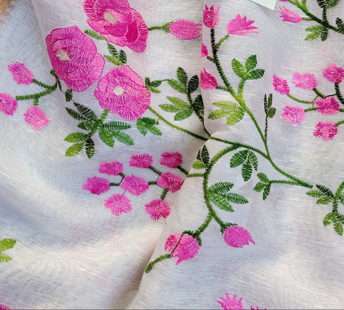 Embroidered fabric with pink flowers and green leaves, featuring a brand tag.