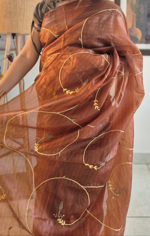 Woman wearing a brown saree with gold patterns indoors.