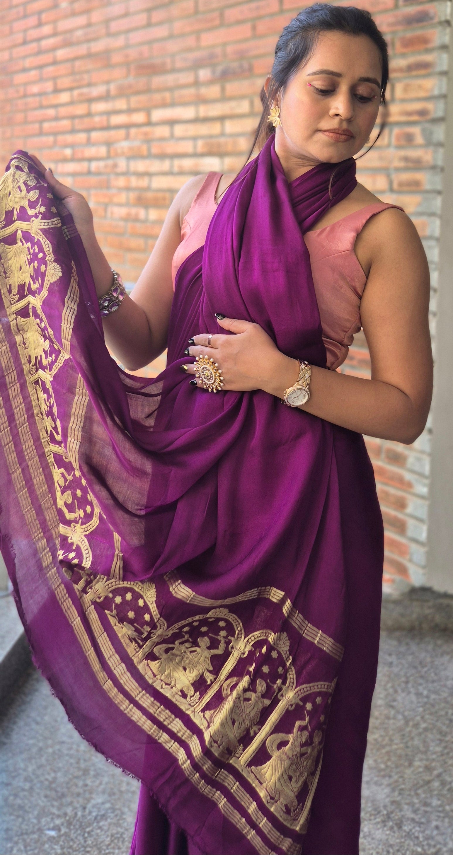 Woman in a purple saree with gold patterns standing indoors.