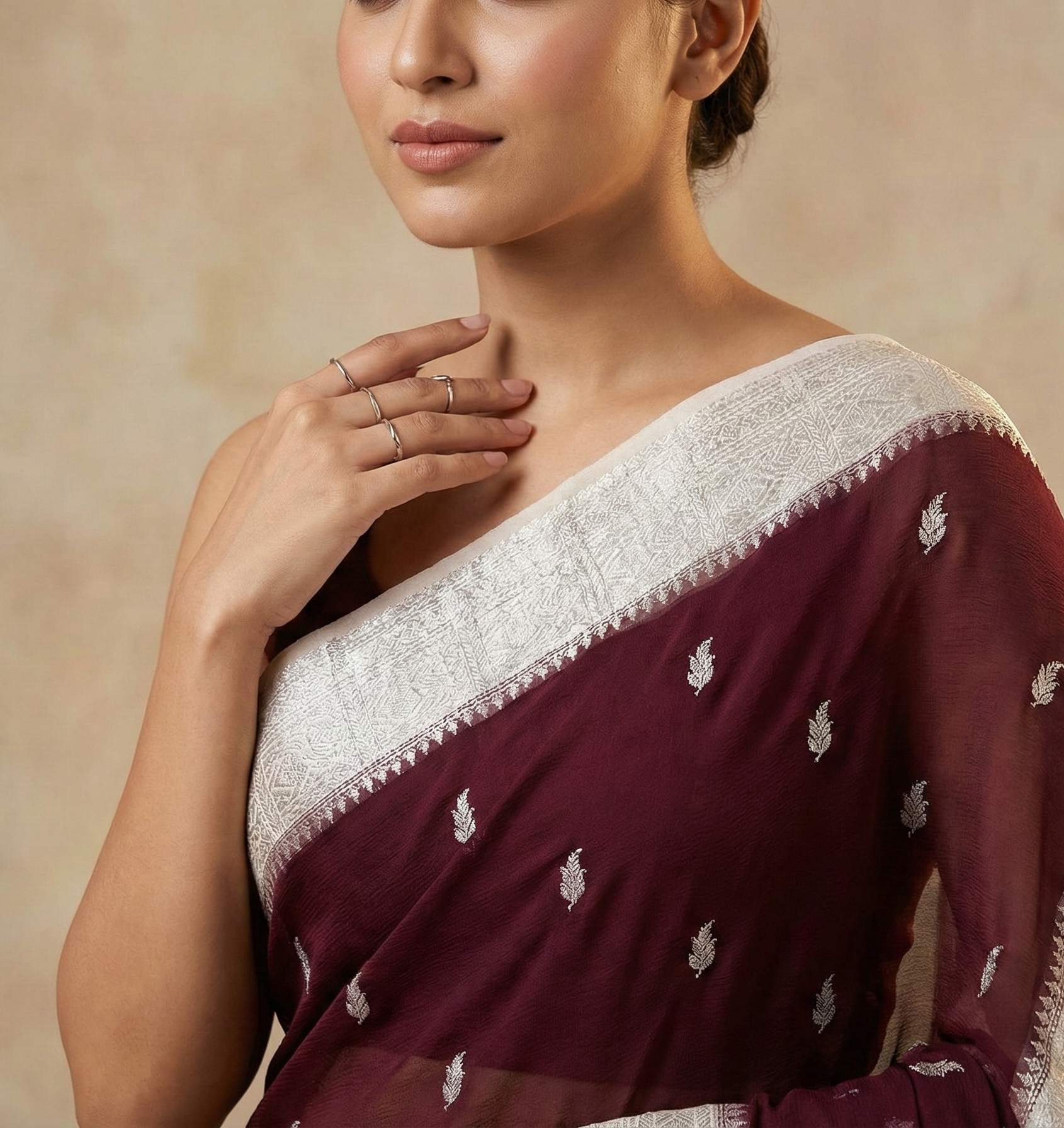 Woman wearing a maroon saree with white embroidery against a beige background