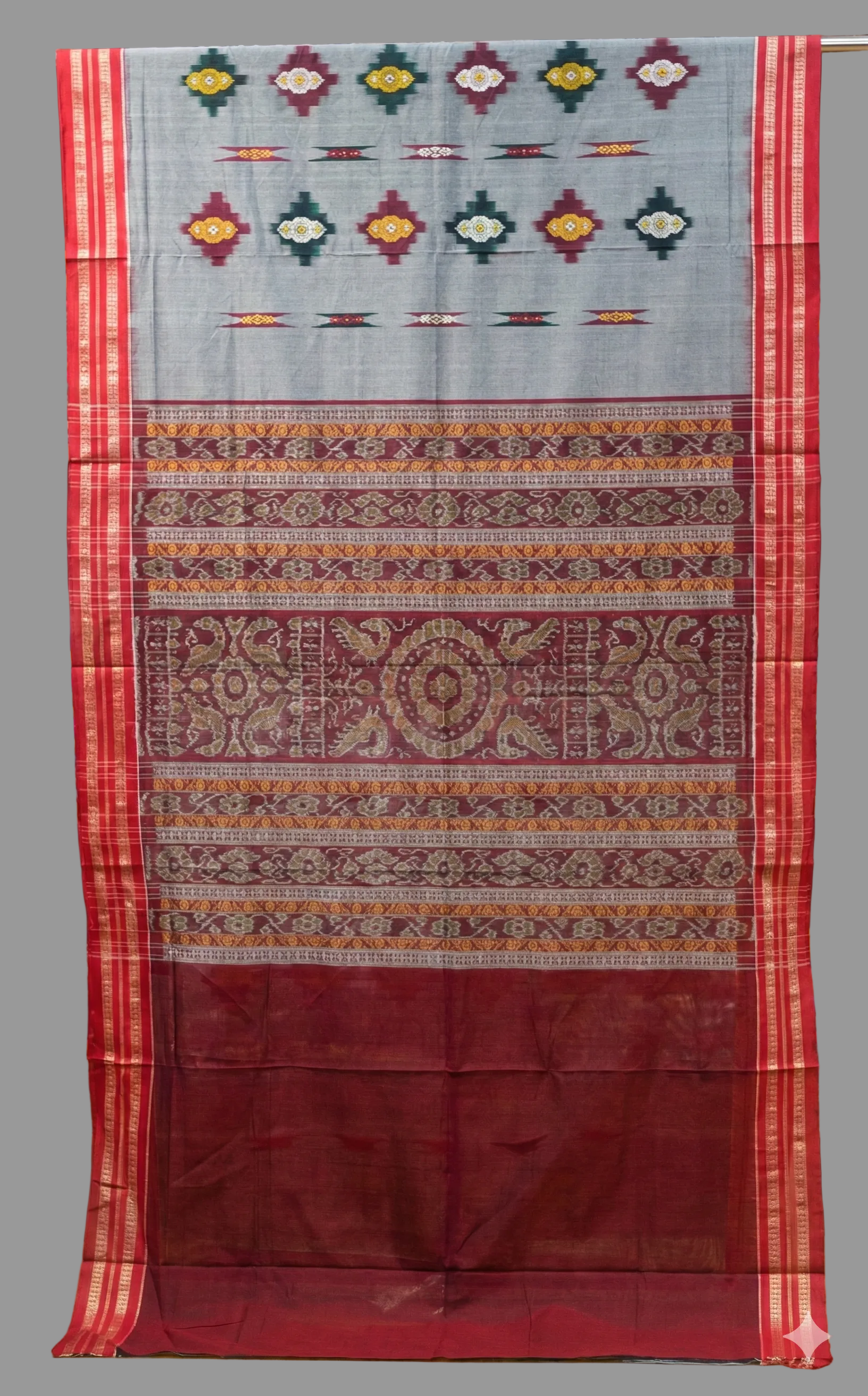 Traditional patterned fabric draped over a rack with shelves of more fabric in the background.
