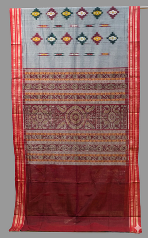 Traditional patterned fabric draped over a rack with shelves of more fabric in the background.